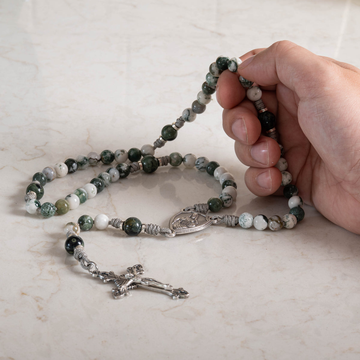 Mystical Rose gemstone rosary held in hand over a marble surface